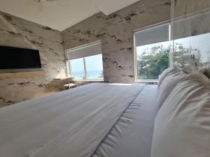 Lotus Rooms@Rockbeach في بونديتْشيري: سرير أبيض في غرفة بها نافذتين
