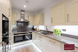 una cocina con armarios blancos y electrodomésticos negros en Sunbury-on-Thames - 4 Bed House en Sunbury Common