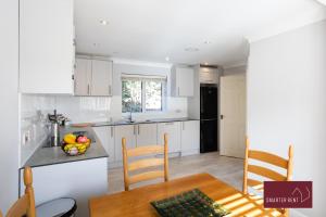 cocina con armarios blancos, mesa y sillas en Wimbledon - 4 Bedroom Home With Parking, Garden & Office en Londres