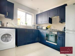 a kitchen with blue cabinets and a washing machine at Knaphill, Woking - 3 Bed House - With Garden in Brookwood