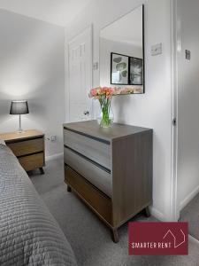 Farnborough - Modern 2 Bedroom House في Blackwater: غرفة نوم مع خزانة مع إناء من الزهور عليها