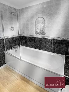 a white bath tub in a bathroom with black tiles at 2 Bed House with Garden, Woking in Chobham