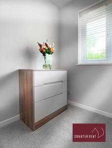 a dresser with a vase of flowers on top of it at Lightwater - 1 Bedroom House - With Parking in Bagshot