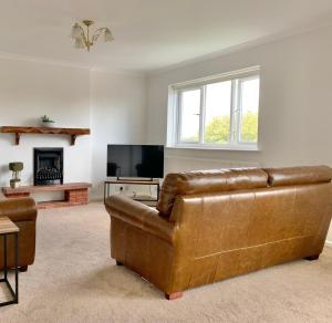 a living room with a brown leather couch and a television at Stratford upon Avon: 2 bed town centre apartment, parking for one car in Stratford-upon-Avon