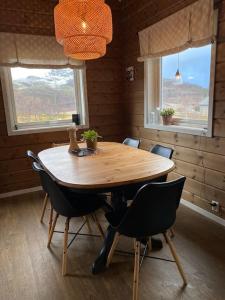 uma mesa de madeira com cadeiras num quarto com duas janelas em Hytte i Neverfjord. em Kvalsund