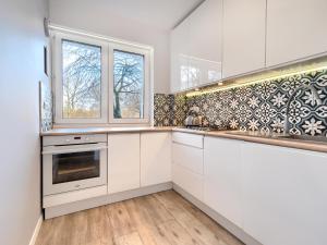 a kitchen with white cabinets and a sink and windows at Platinium Zaspa - Pilotów 14 in Gdańsk