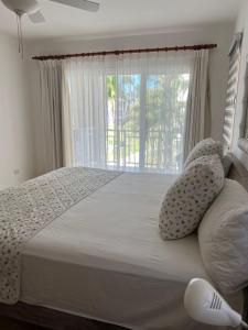 ein Schlafzimmer mit einem Bett mit Kissen und einem Fenster in der Unterkunft Bello y cómodo apartamento, frente al mar in Punta Cana