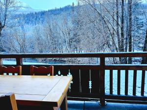 einen Holztisch auf einem Balkon mit schneebedeckten Bäumen in der Unterkunft La rivière d'argent T3 Serre Chevalier Pied des pistes in Saint-Chaffrey