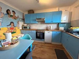 a kitchen with blue cabinets and a table with a basket of food at Fun family beach house! in Lessingham