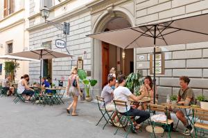 um grupo de pessoas sentadas em mesas sob guarda-chuvas em Ostello Bello Firenze em Florença