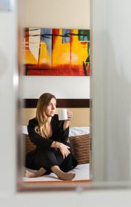 une femme assise sur un lit tenant une tasse de café dans l'établissement Gladstone Heights Executive Apartments, à Gladstone