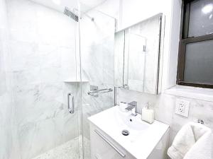 La salle de bains blanche est pourvue d'un lavabo et d'une douche. dans l'établissement 62-2B Renovated 1BR in Prime Upper East Side, à New York