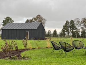 Tre sedie in un campo con un fienile nero di Viesuli Village Villa a Saraiķi