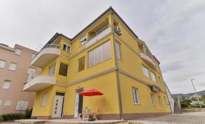 een geel gebouw met een rode paraplu ervoor bij Apartmani Castrum in Kaštela