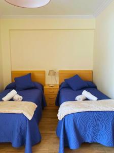 una camera con 2 letti con lenzuola blu e comodino di Apartamentos Melgarden - Campo del Marqués a Santoña