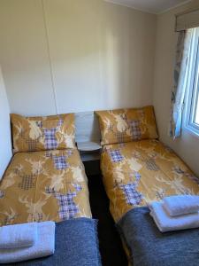Cette chambre comprend deux lits et une table avec une fenêtre. dans l'établissement Family Caravan, Seton sands, Haven holiday village, à Port Seton