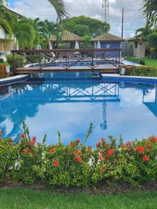 a swimming pool with blue water and red flowers at Village Verano Guarajuba in Guarajuba