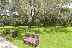 a park bench sitting in the grass under a tree at Lovely Lakeside 4-Bed Pool Home at Villa Sol-3125 in Kissimmee