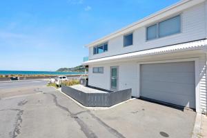 a white house with a garage next to the ocean at Lyall Bay Parade Apartment in Wellington