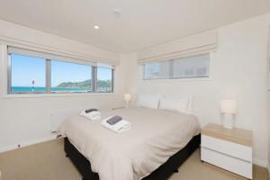 a white bedroom with a large bed and windows at Lyall Bay Parade Apartment in Wellington