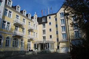 Un grand bâtiment jaune avec des drapeaux en haut dans l'établissement Hotel Rheinischer Hof Bad Soden, à Bad Soden am Taunus