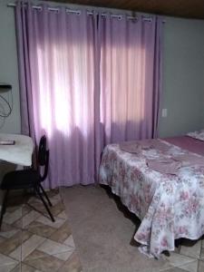 a bedroom with a bed and a window with pink curtains at Pousada Maria Rosa in Blumenau