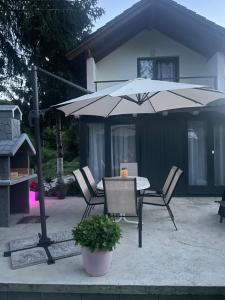 a table and chairs under an umbrella in front of a house at Vikendica u prirodi na ranču in Zolaći
