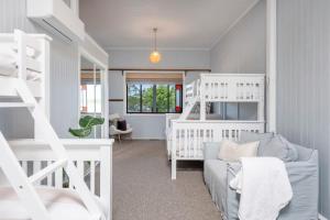 a bedroom with white bunk beds and a couch at Riverside Ranch - oceanstays in Yamba