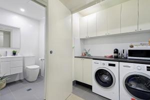 a white kitchen with a washer and dryer in it at The Beach Studio in Huskisson