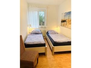 2 Betten in einem Zimmer mit einem Stuhl und einem Fenster in der Unterkunft Holiday apartment sea air in Langeoog