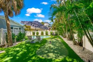 a yard with chairs and an umbrella and palm trees at The Cottage on Pine - Luxury Boho Beach Cottage wPvt Heated Pool On Pine Ave in Anna Maria