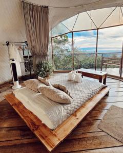 een groot bed met kussens in een kamer met ramen bij El Mirador Glamping & Apartments & Woodhouse & Swimingpool in Miramar