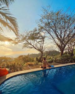 un hombre sentado en el borde de una piscina en El Mirador Glamping & Apartments & Woodhouse & Swimingpool en Miramar