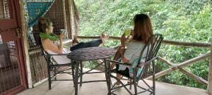 dos mujeres sentadas en una mesa en un porche con bebidas en Stilts Diani Beach, en Diani Beach