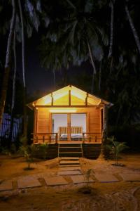 Cabaña de madera pequeña con porche por la noche en The Pearl Beach Resort en Canacona