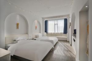 a white room with two beds and a window at Wuzhen Qiuxi Art Hotel in Tongxiang