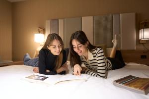 zwei Mädchen, die auf einem Bett liegen und ein Buch lesen in der Unterkunft Hotel Resol Kyoto Shijo Muromachi in Kyoto