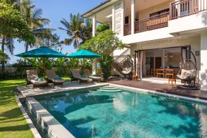 a swimming pool with chairs and umbrellas next to a house at Villa Sanika in Candidasa