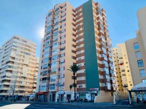 un edificio alto con una palmera delante de él en Playa La Cortadura & Parking FREE Grupo AC Gestion, en Cádiz