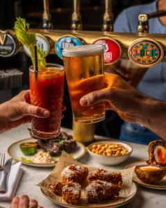 dos personas sosteniendo vasos de bebidas en una mesa con comida en The William, en Londres