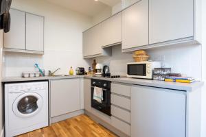 cocina con armarios blancos, lavadora y secadora en Flat w/ Balcony & Canal view - 4min to station, en Dublín