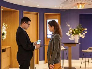 a man and woman standing in a lobby looking at a cell phone at Mercure Paris Opera Garnier Hôtel & Spa in Paris