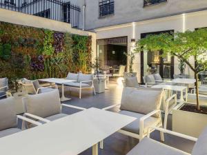 un restaurante con mesas blancas, sillas y plantas en Mercure Paris Opera Garnier Hôtel & Spa, en París