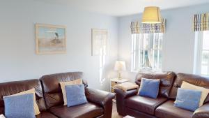 a living room with brown leather couches and blue pillows at Willow Cottage - Part of the The Bay Filey Holiday Village with pool, gym and direct beach access, pub, restaurant, tennis and meadows walks in Reighton +49 photos