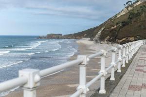 ein weißer Zaun neben einem Strand mit Meer in der Unterkunft Apartamento La Vega de Santiago 2 in Posada de Llanes