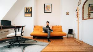 un homme assis sur un canapé orange dans un salon dans l'établissement 4-Schlafzimmer-Terrassensuite Oasis - WORKSPACE EM-APARTMENTS DEUTSCHLAND, à Bielefeld