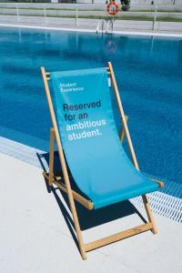 un cartel sentado en una silla junto a una piscina en Student Experience Madrid Pozuelo - Luxury Hostel, en Pozuelo de Alarcón