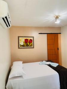 Pousada Recanto das Orquídeas في باريرينهاس: غرفة نوم بسرير ابيض ولوحة ورد