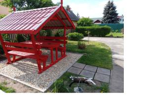 un banco del parque rojo con un perro tirado en el césped en SZIESZTA APARTMAN, en Gárdony