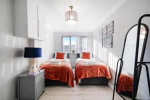 Spacious, 4 bed, Garden, Parking, ExCel London في لندن: سريرين في غرفة بجدران بيضاء وملاءات برتقالية